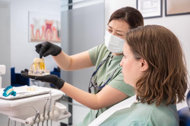 A woman is sitting in a dental chair while a dentist shows her a model of her teeth.