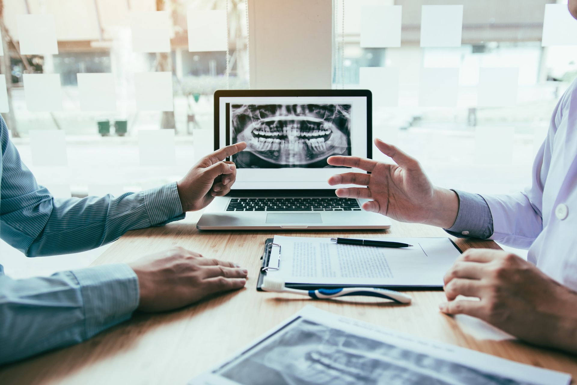 Dentist and patient looking at dental X-rays on a laptop at a desk.