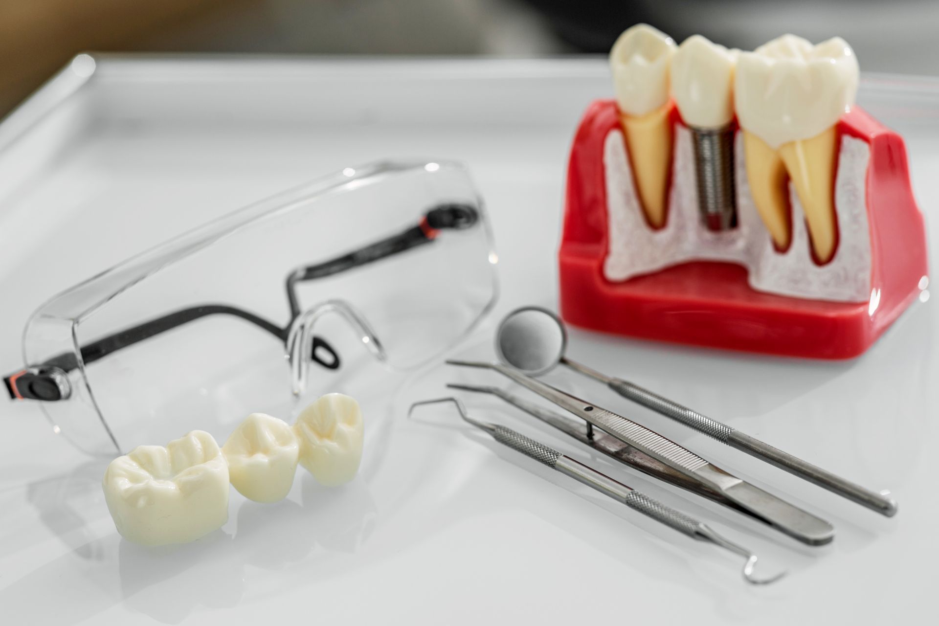 Dental tools, model teeth, safety glasses on a white surface, illustrating dental implants and procedures.