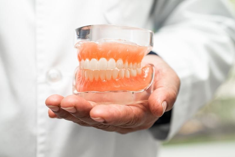 A dentist is holding a model of permanent dentures in his hand