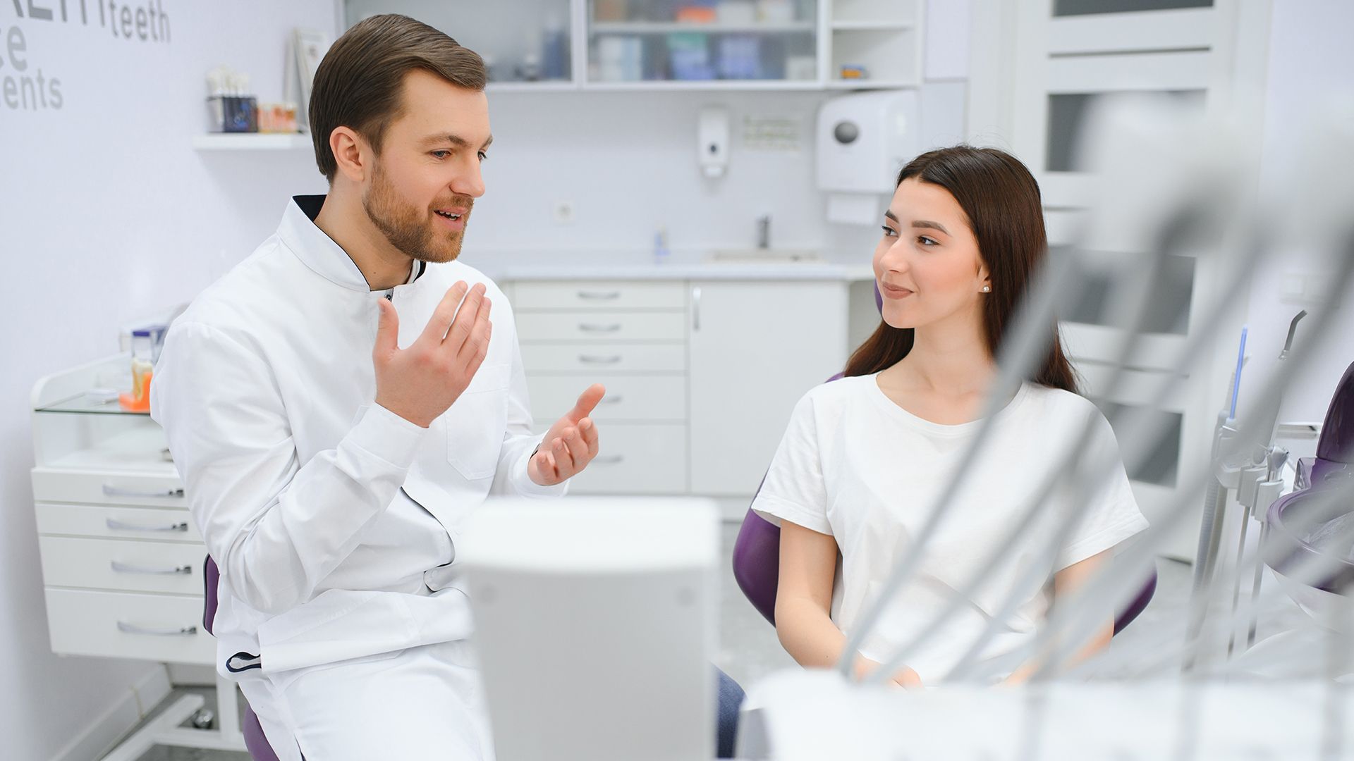 A dentist in a white coat speaks to a patient in a dental chair