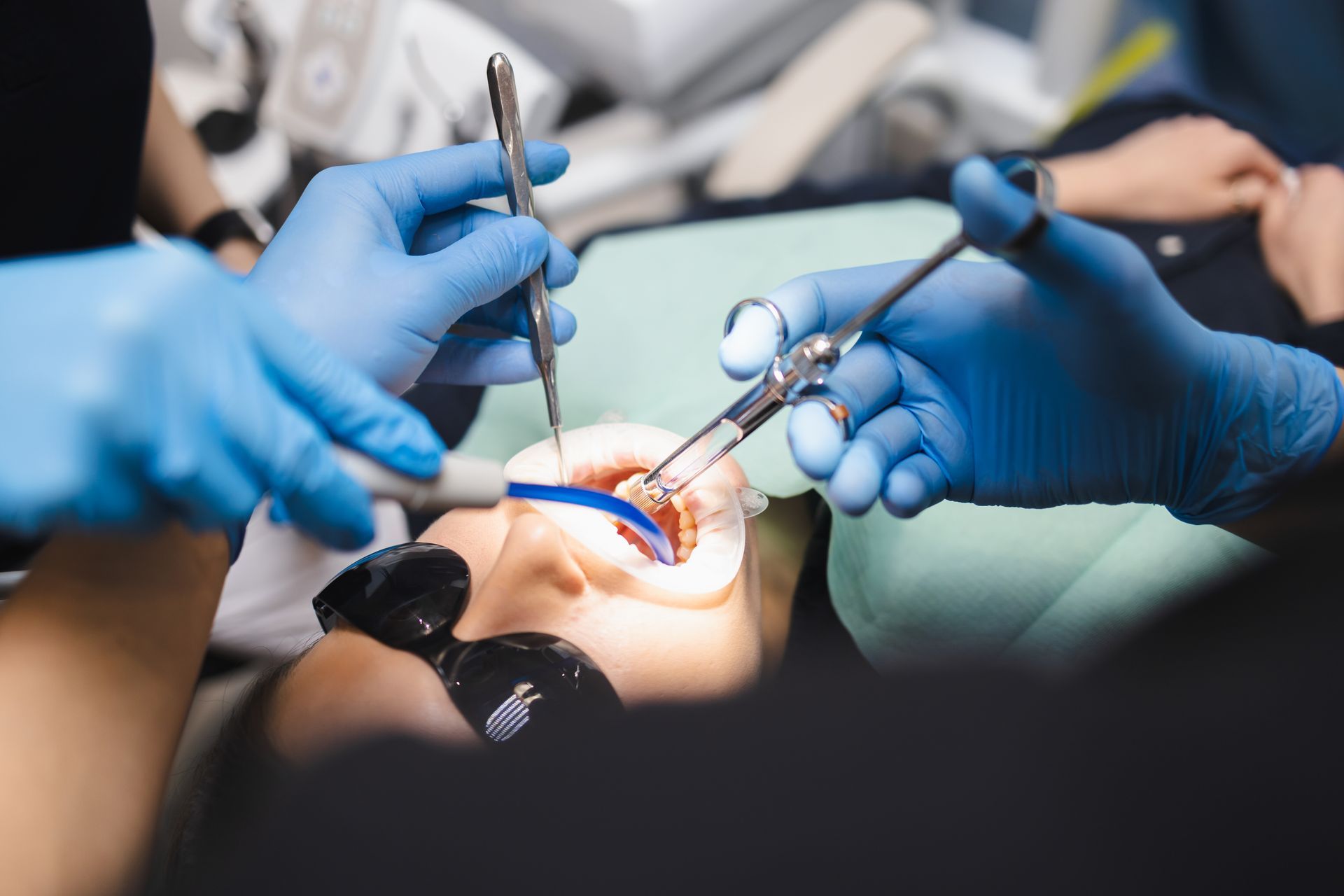 Dentist using tools to treat a patient’s teeth, with blue-gloved hands in a clinic booth