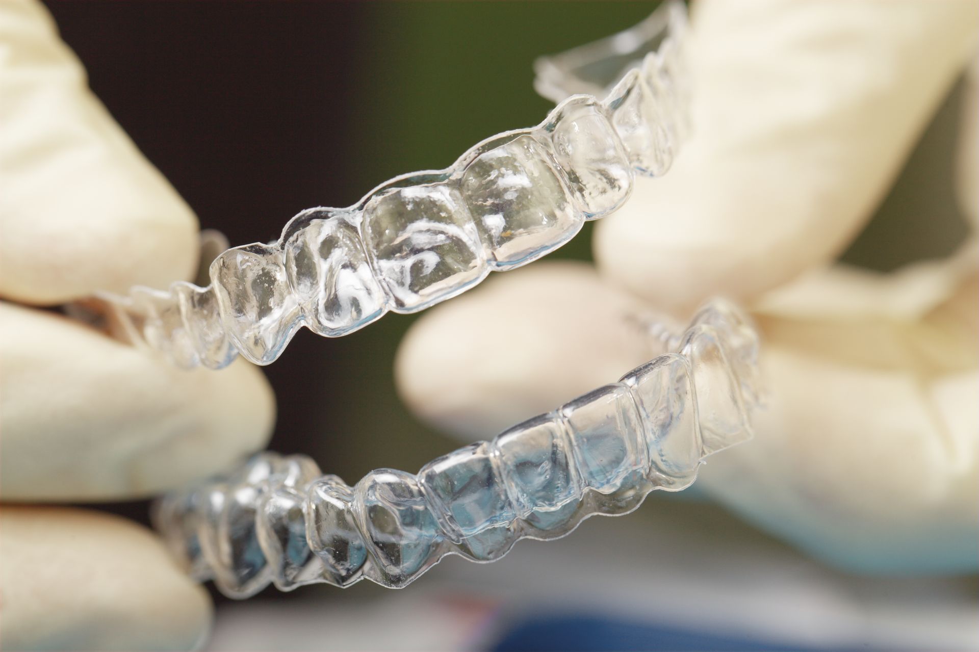 Clear Invisalign aligners held by gloved hands.