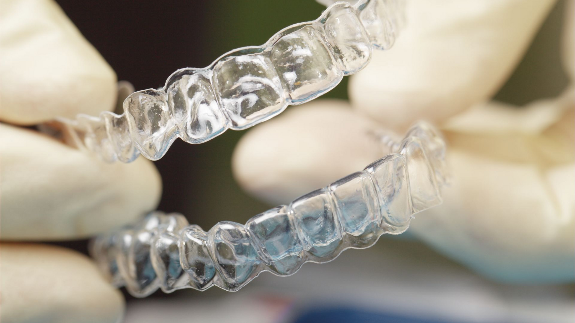 Clear aligners, held by gloved hands, for teeth straightening.