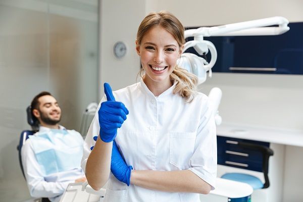 A female dentist is giving a thumbs up in a dental office.