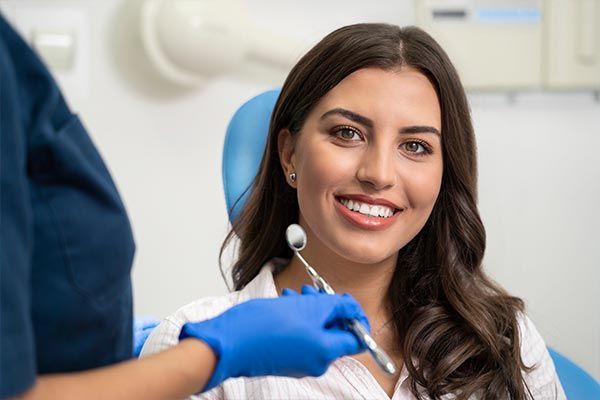 A woman is sitting in a dental chair while a dentist examines her teeth.