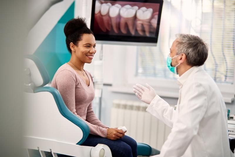 A woman is sitting in a dental chair talking to a dentist.