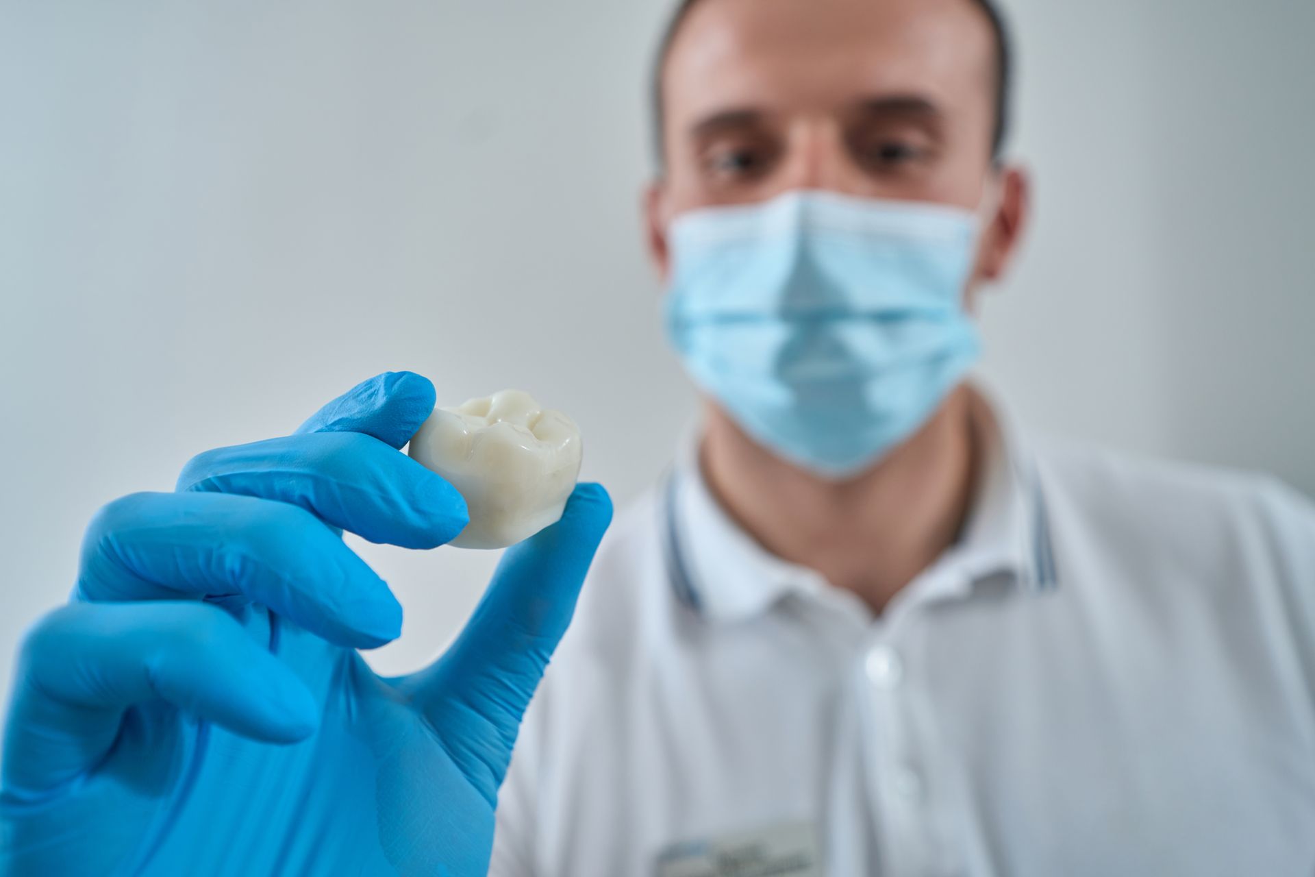 Blue-gloved worker holding a small white dental mold while wearing a surgical mask