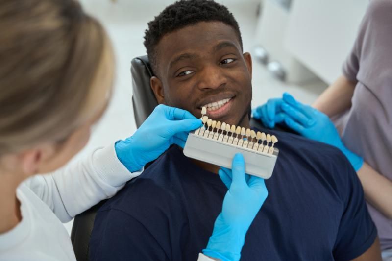 A man is sitting in a dental chair while a dentist examines his teeth.