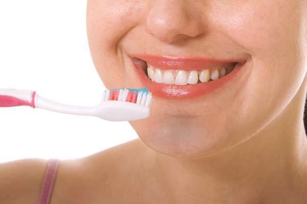 A woman is brushing her teeth with a pink toothbrush