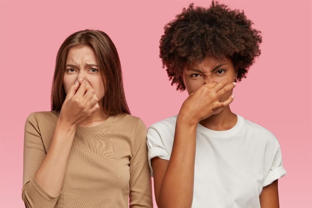 Two women are covering their noses with their hands because of bad breath