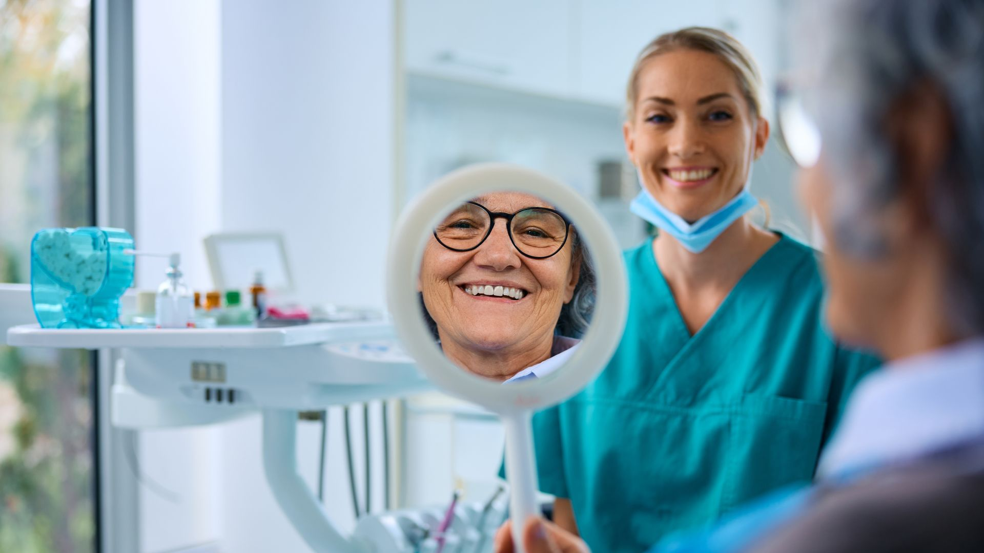 Dentist showing a smiling elderly patient her teeth in a mirror. Dental office setting.