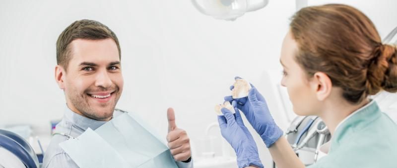 A man is giving a thumbs-up while sitting in a dental chair.