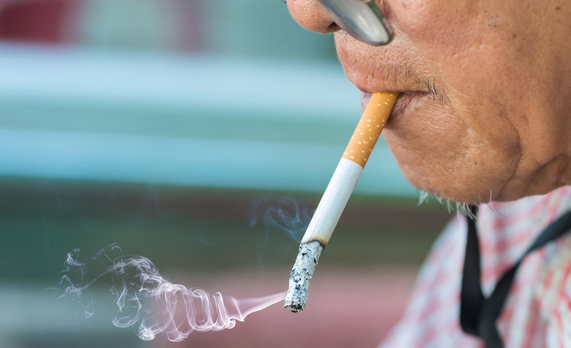 Close-up of a person smoking a cigarette, with smoke drifting in front of a blurred background.