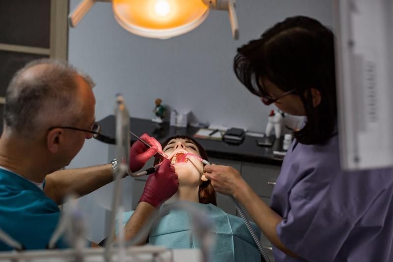 A woman is getting her teeth examined by a dentist and a nurse in a dental office.