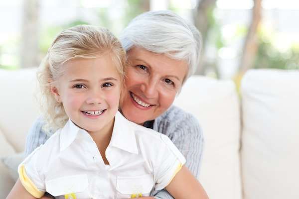 An elderly woman is hugging a little girl on a couch.