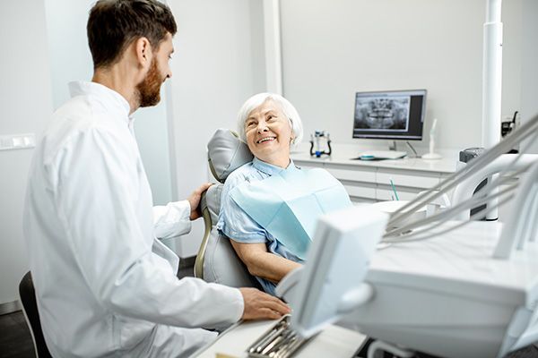 A dentist is talking to an elderly woman in a dental chair.