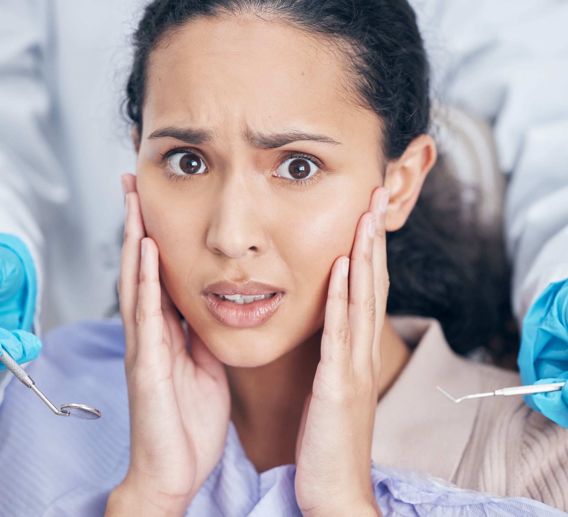 Nervous patient with hands on cheeks, surrounded by dentists holding tools in a dental office