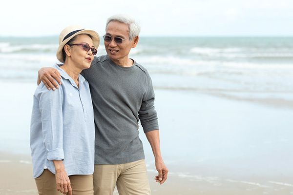 An elderly couple is walking on the beach.