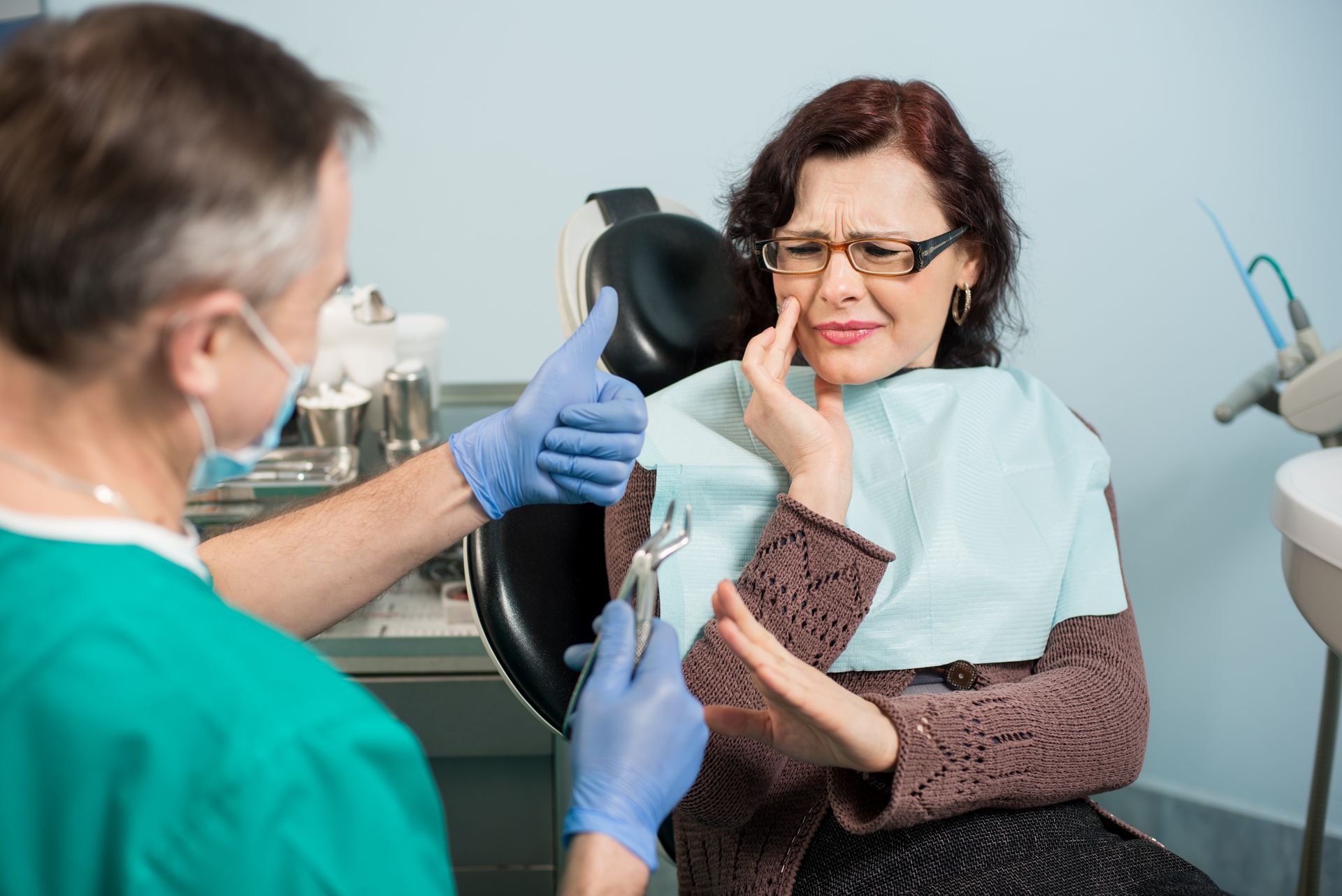 Dentist prepares to extract a tooth from a distressed woman in a dental office.