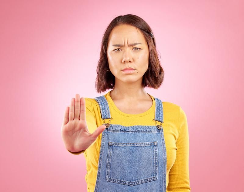 A woman in overalls is making a stop sign with her hand.