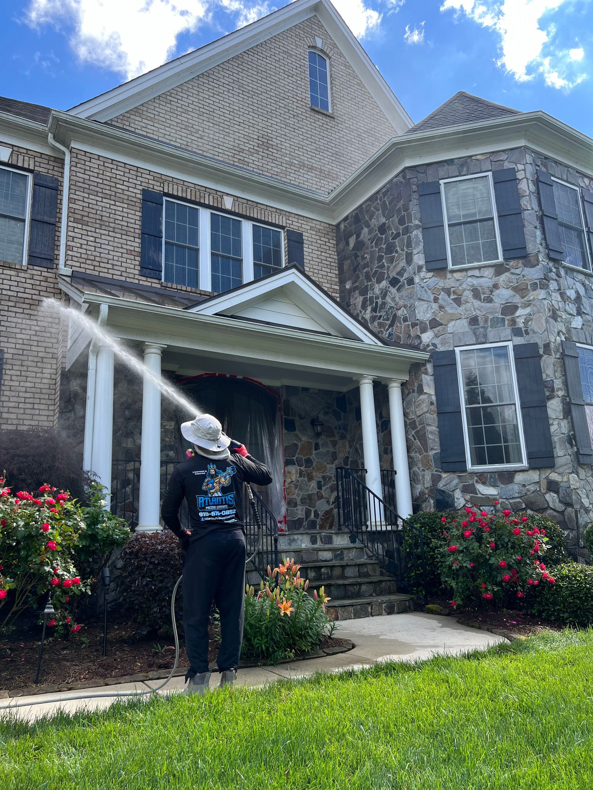 A man is cleaning the front of a large brick house with a pressure washer.