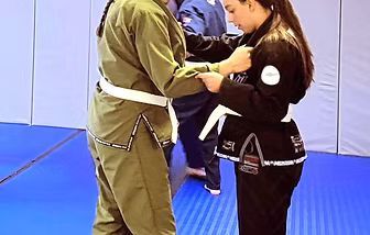 Two people in martial arts uniforms practice a move on a blue mat.