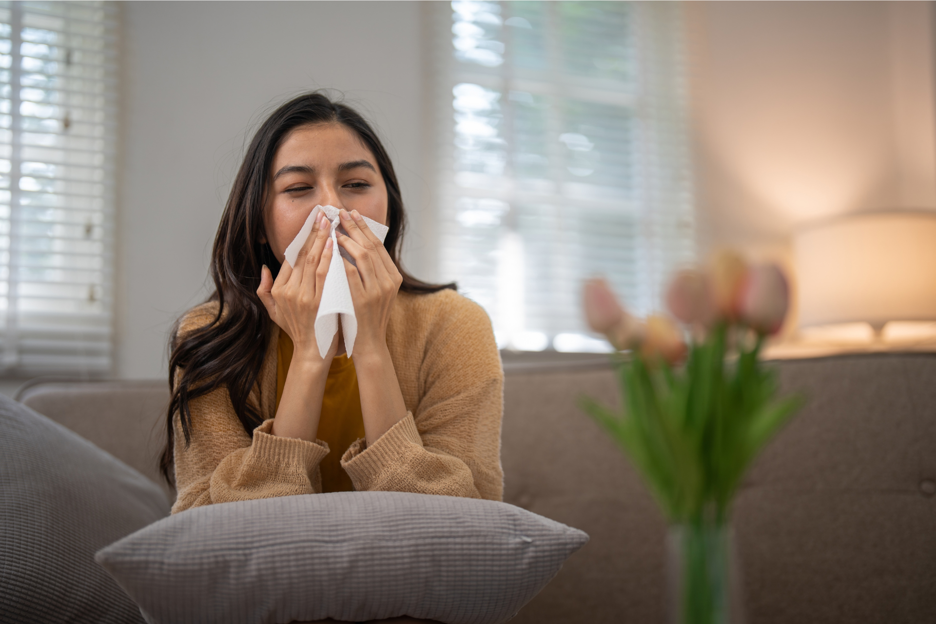 A woman is blowing her nose into a napkin while sitting on a couch.