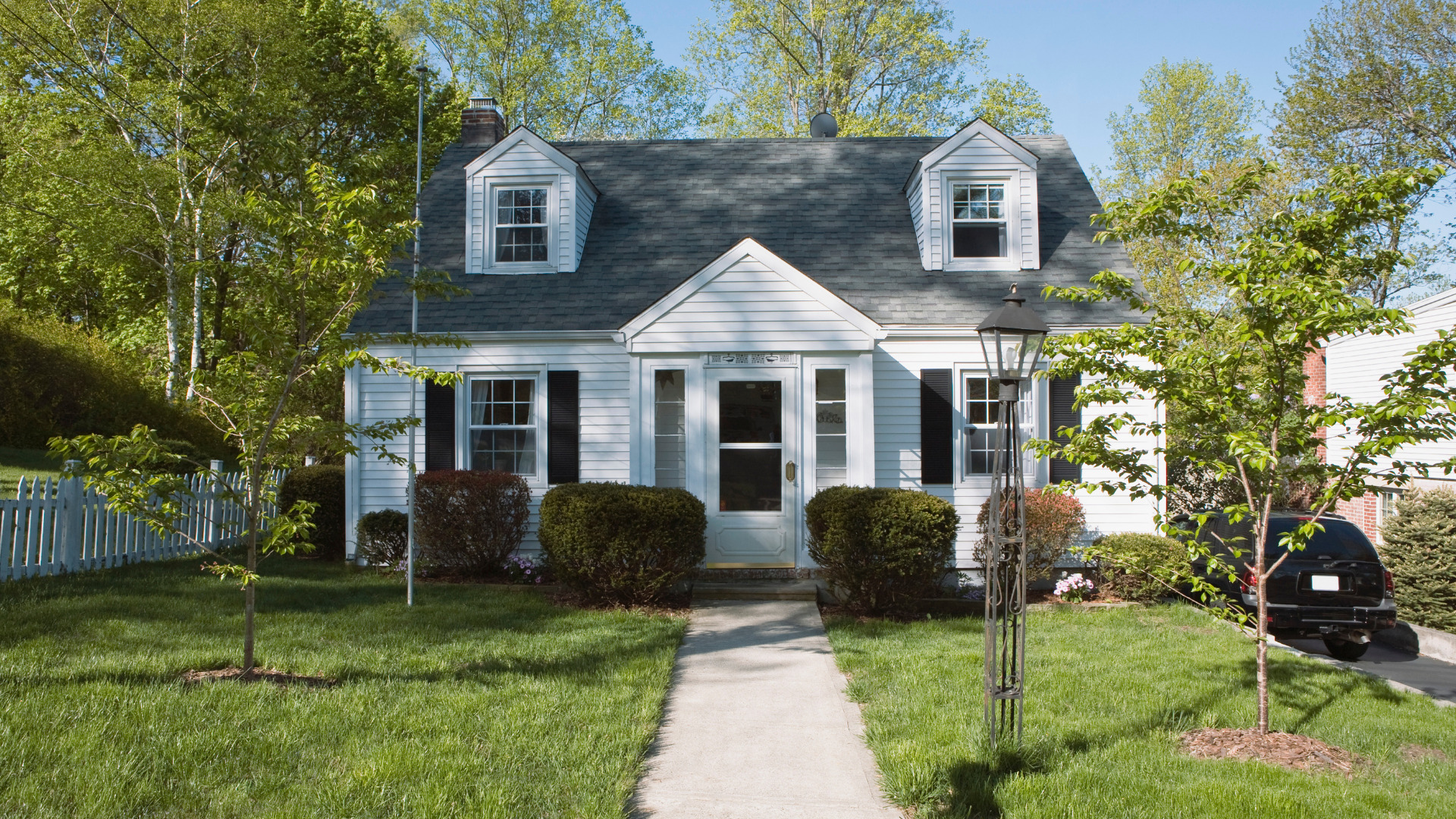 White cottage with gray roof, two dormers, and a sidewalk leading to the front door.