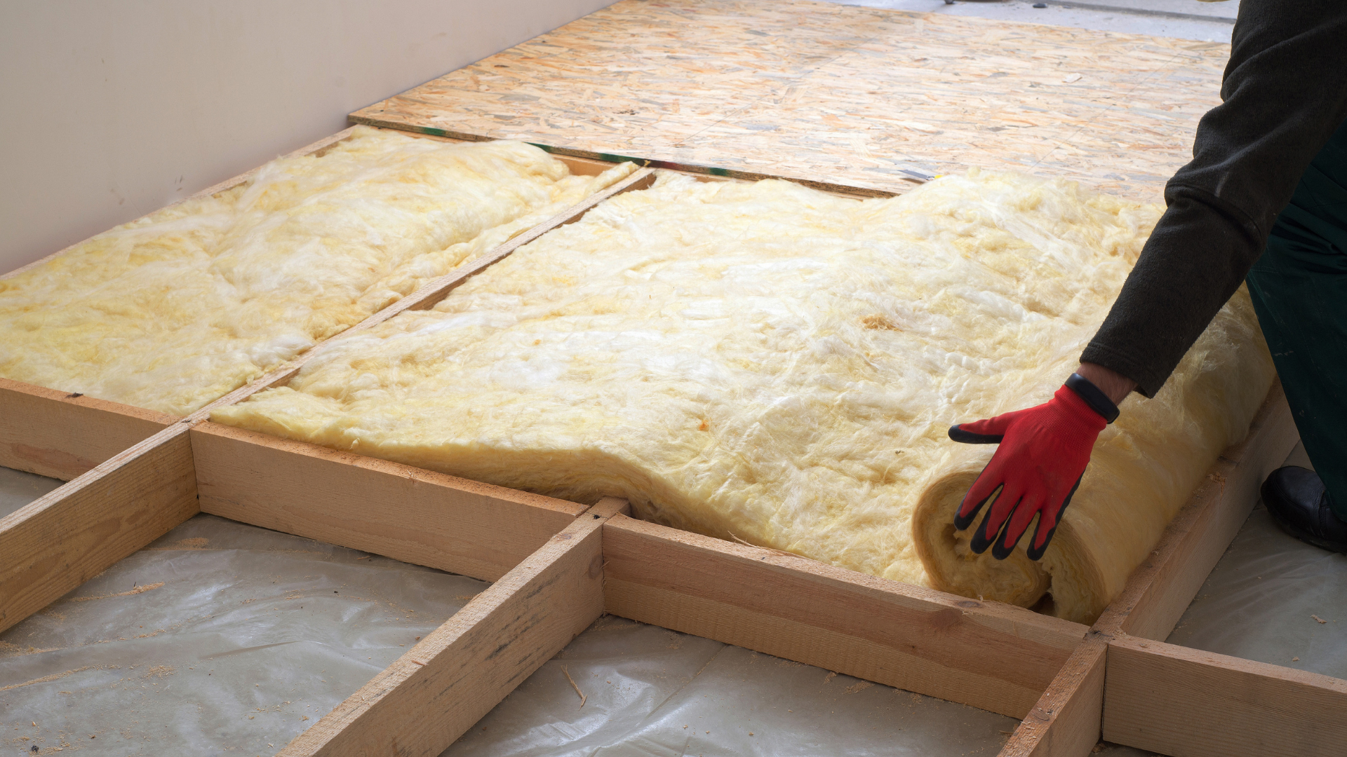 Person installing insulation between wooden floor joists.