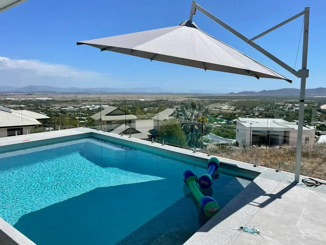 Modern swimming pool with cantilever umbrella overlooking a city.