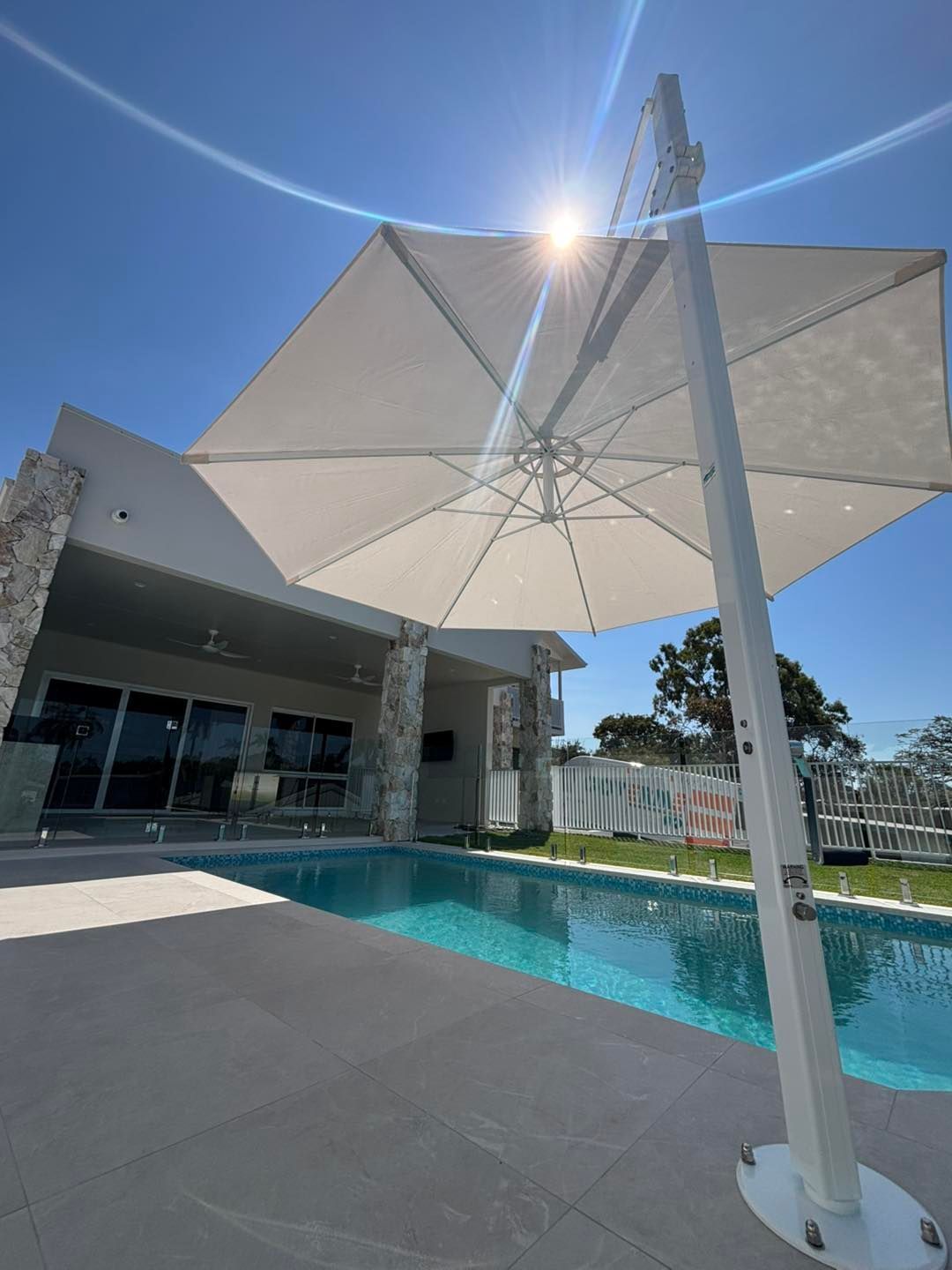 Pool with turquoise water, a pink float, and black umbrella providing shade. White buildings are in the background.