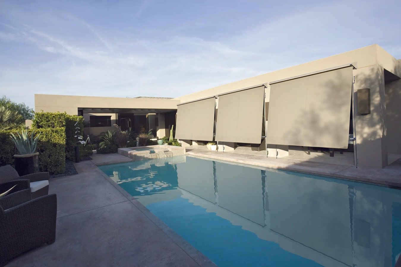 Swimming pool and patio of a modern home; retractable awnings; blue water; sunny day.