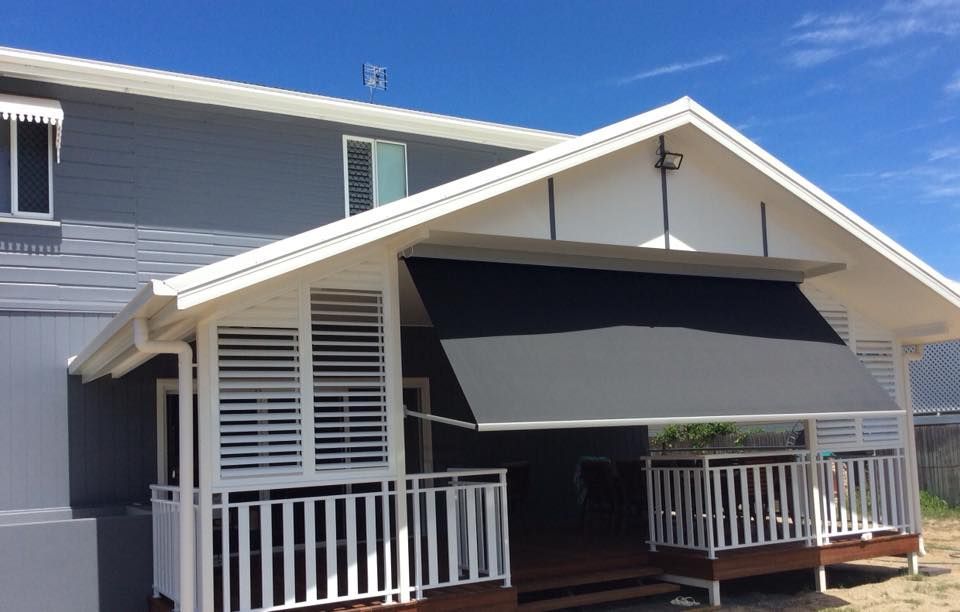 Two-story house with a white porch featuring a retractable gray awning and white shutters, under a blue sky.