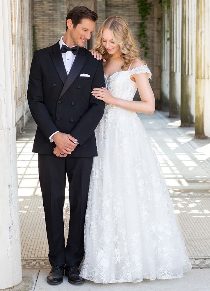 Groom in black tuxedo with bride in white gown posing by columns.