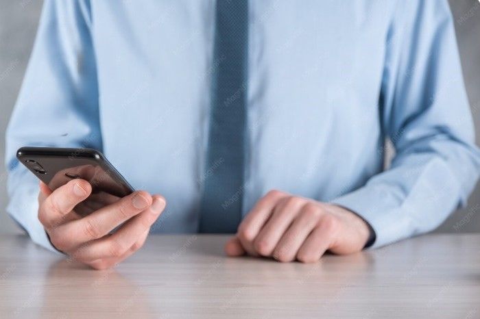 Persona con camisa azul claro sosteniendo un teléfono inteligente en una mesa.