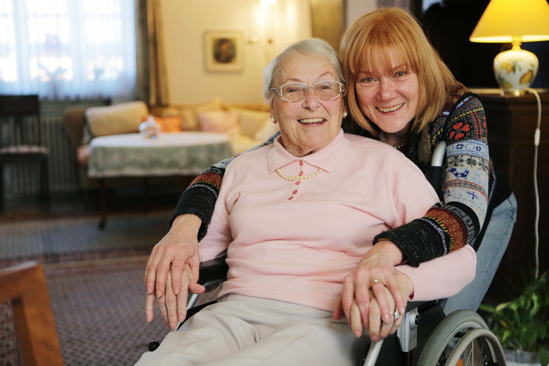 Woman smiling beside an elderly person in a wheelchair, demonstrating a guardianship.
