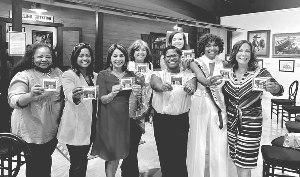 A group of women are standing next to each other holding pictures in a black and white photo.