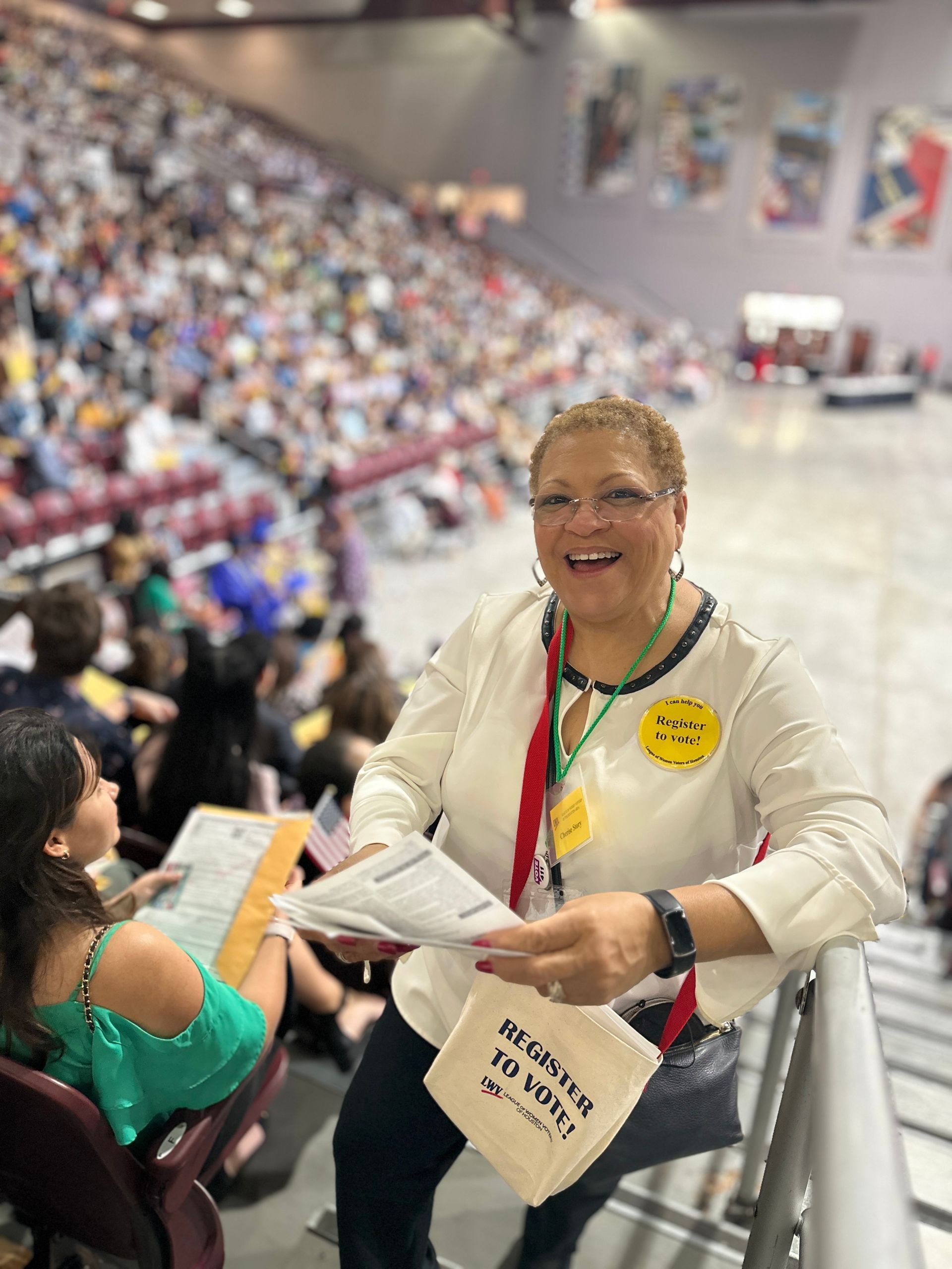 A woman is sitting on a railing in a stadium holding a bag.