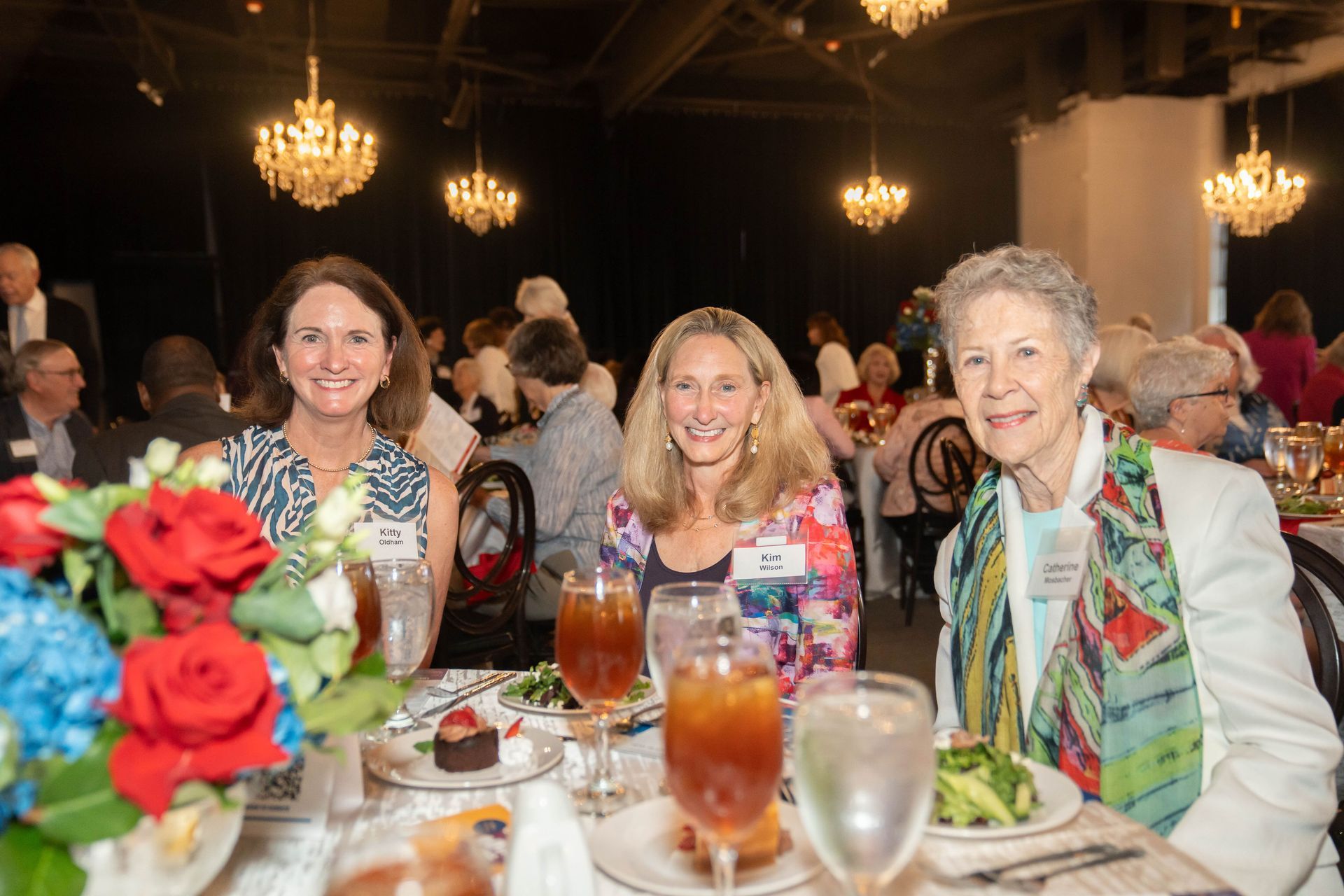 Three women are sitting at a table with plates of food and glasses of water.