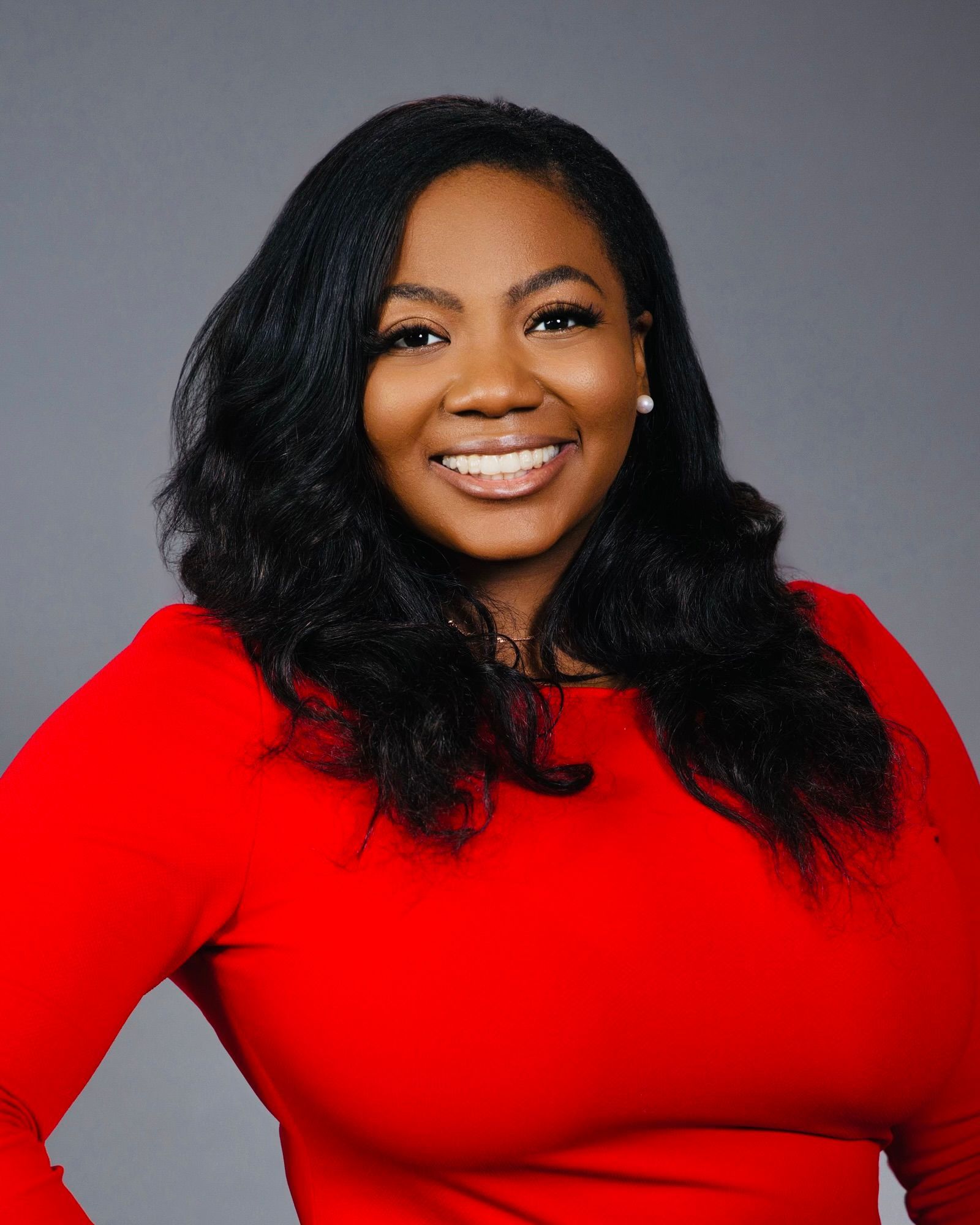 Woman with dark hair smiling broadly in a red top against a gray background.