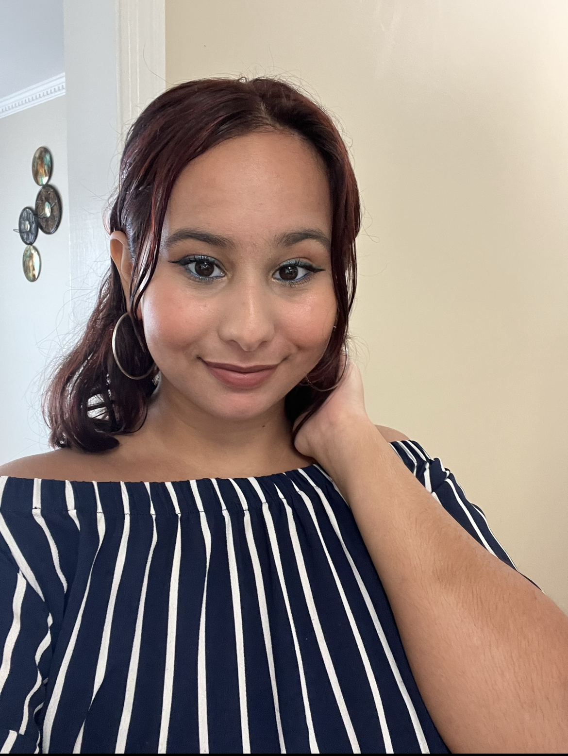 Woman with reddish-brown hair wearing an off-the-shoulder striped top and hoop earrings, smiling at the camera.