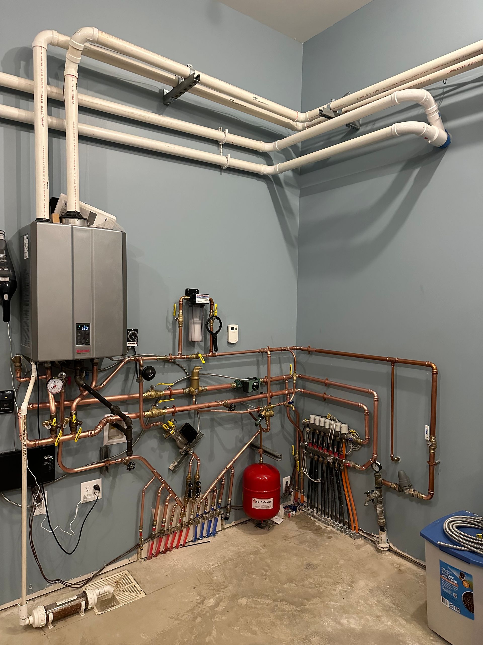 A room with a lot of pipes and a boiler on the wall.