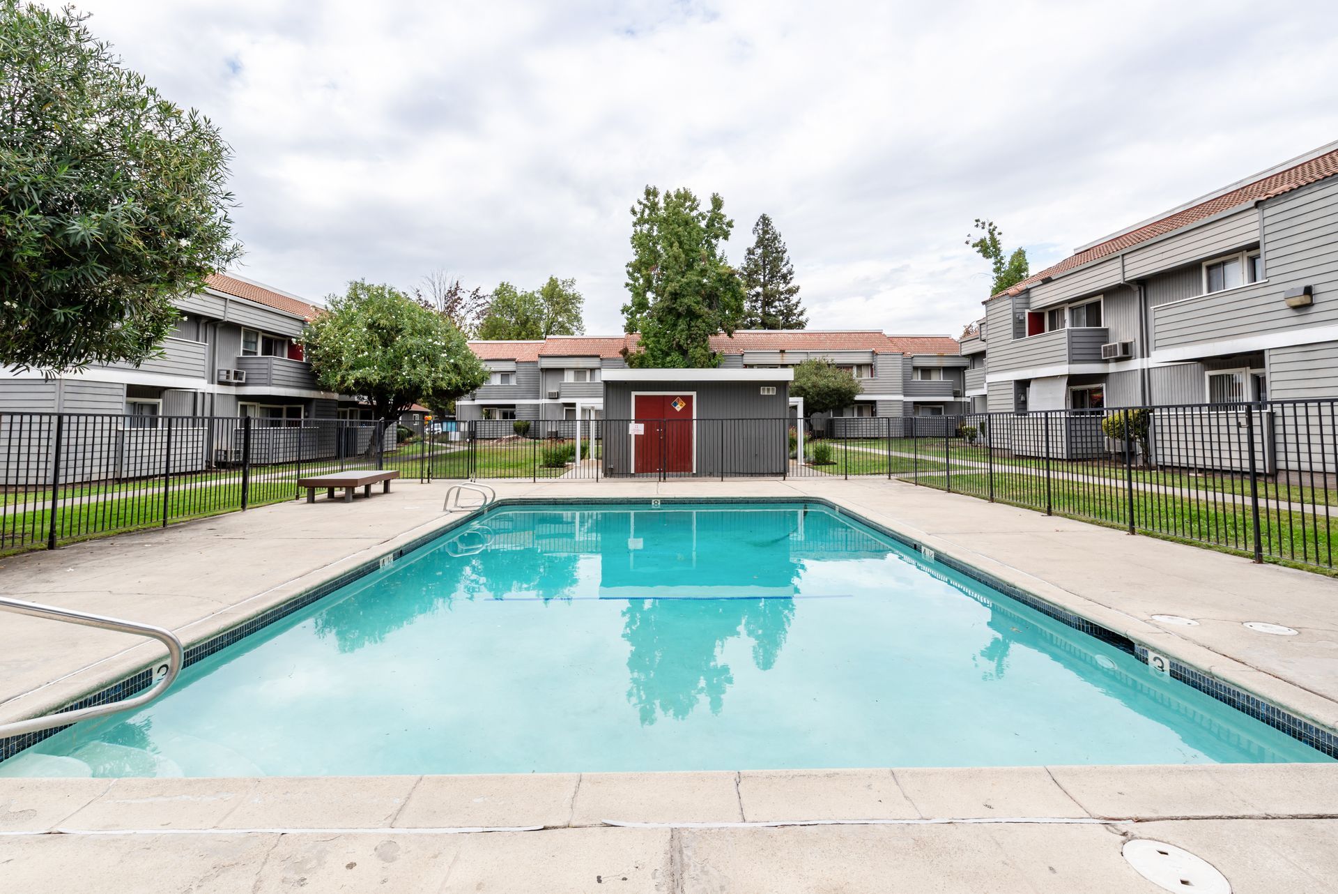 Swimming pool in a complex with buildings and a small shed. Gray buildings, pool has blue water.