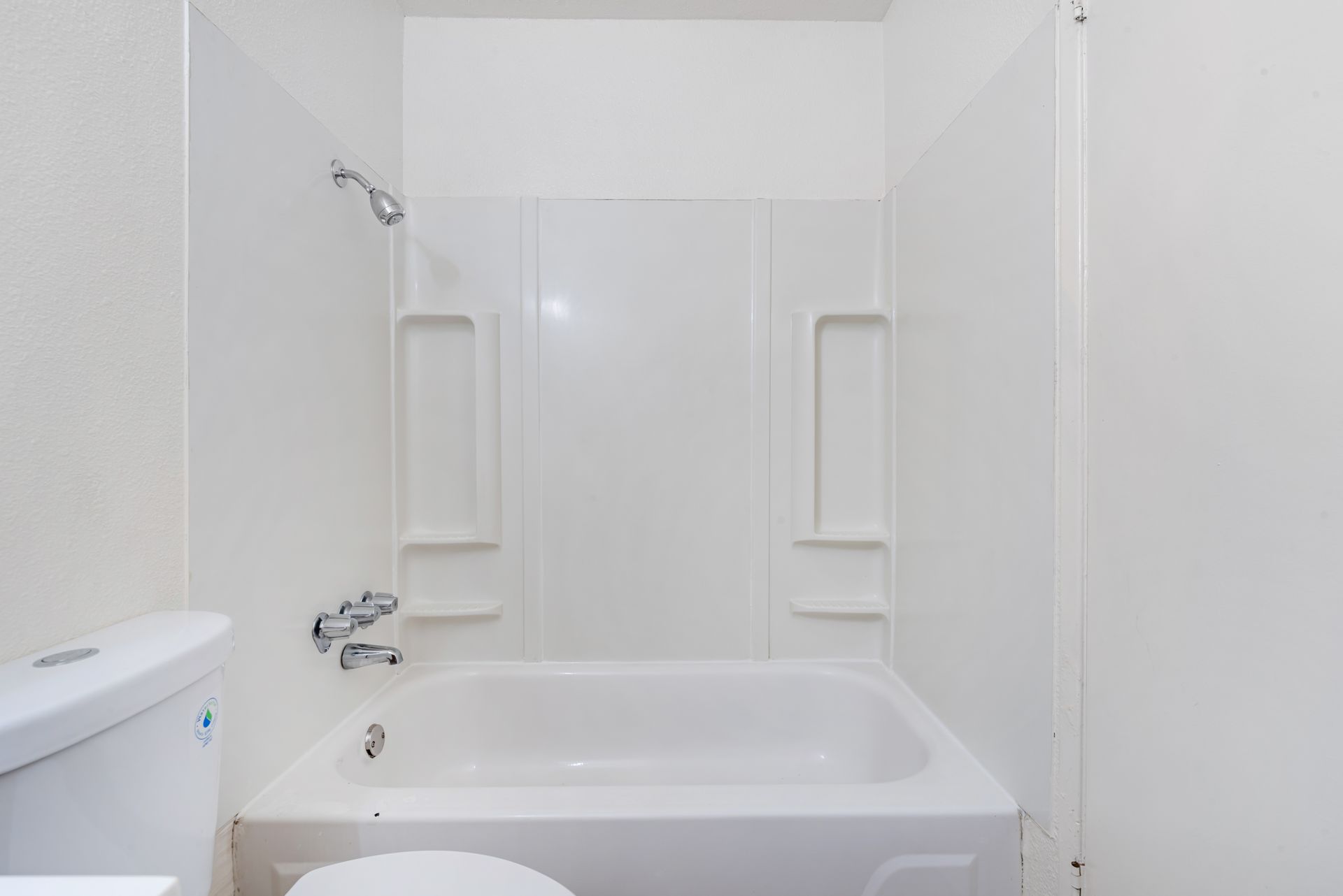 White bathroom with a bathtub, showerhead, and toilet.