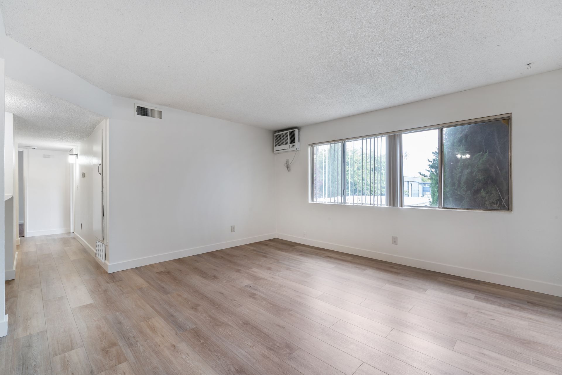 Empty apartment interior with wood flooring, white walls, and a window.