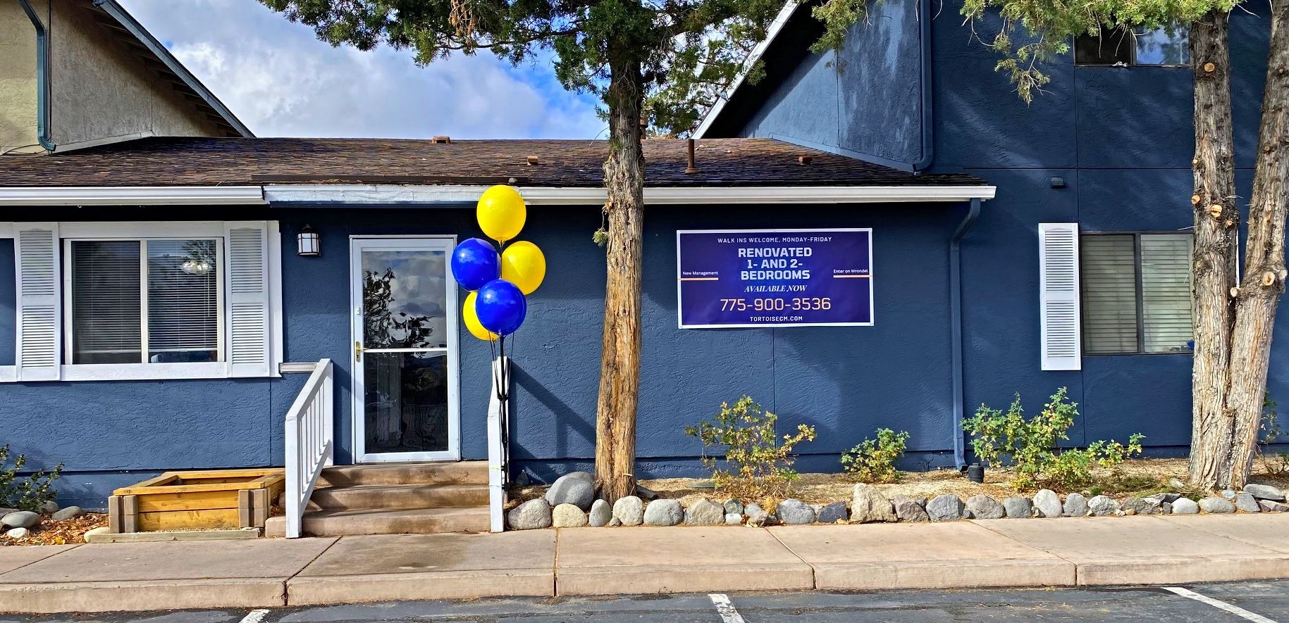 Blue building with balloons, sign, and tree.