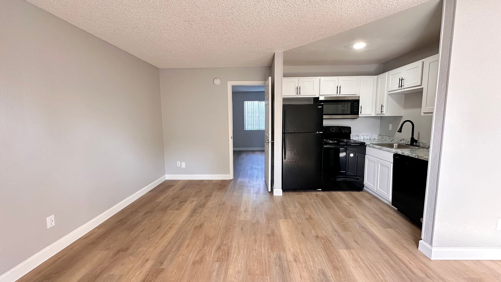 Open apartment interior with wood floors, light gray walls, and a small kitchen.