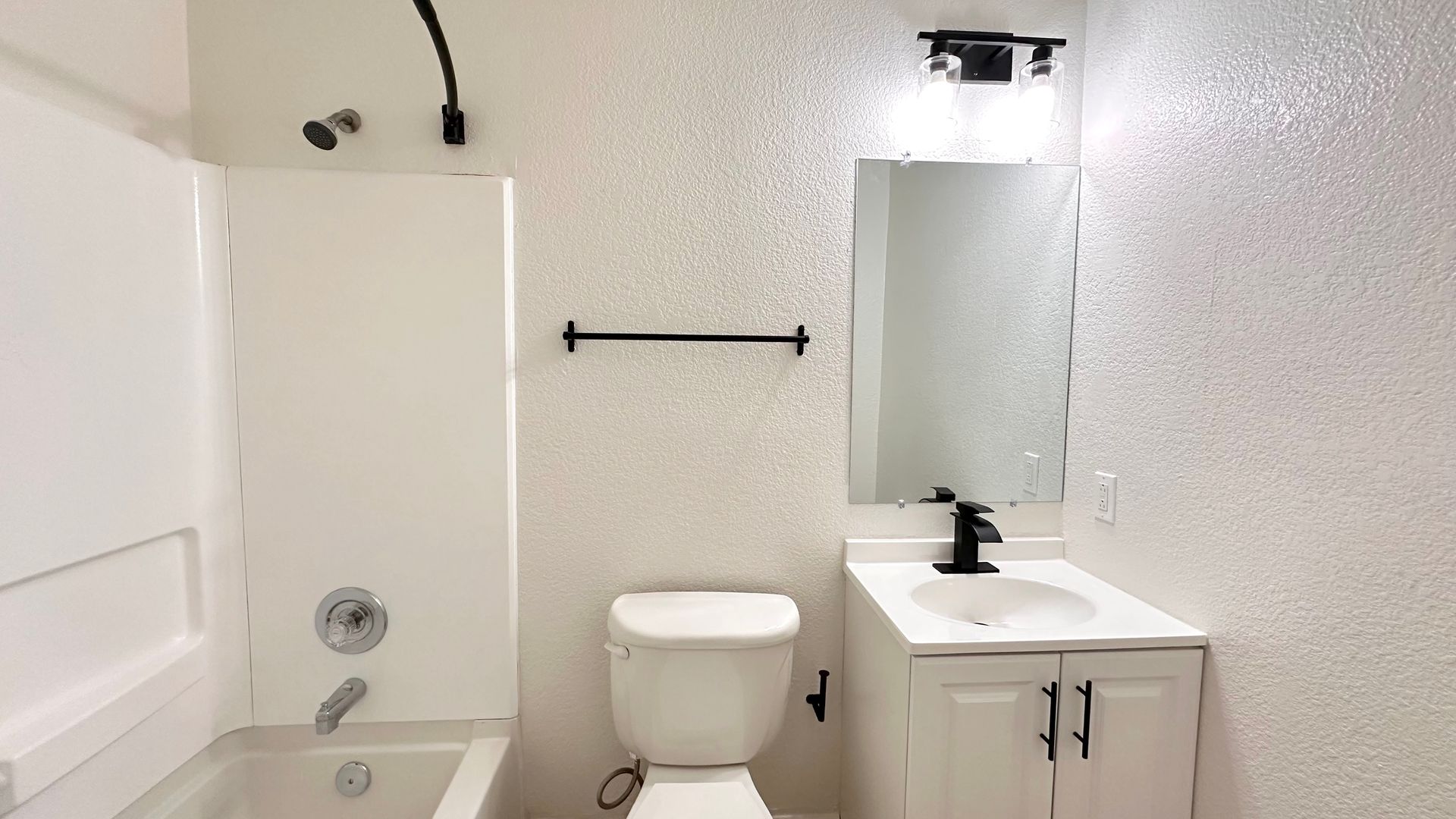 White bathroom with a bathtub, toilet, sink, mirror, and glittery wall. Black fixtures.