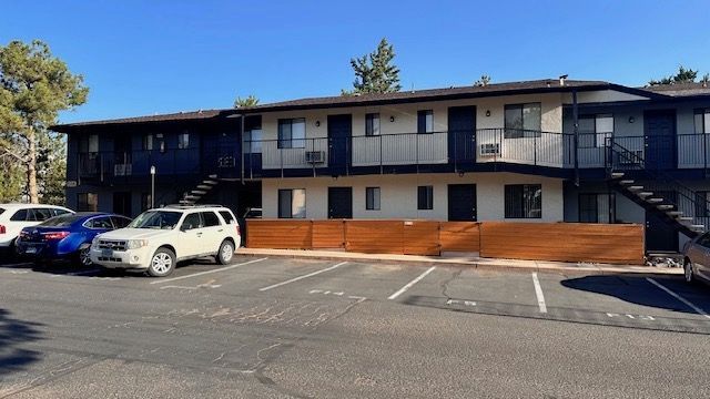 Two-story apartment building with parking, blue and white exterior. Cars parked in front. Sunny day.